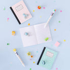 Notebooks, pens, and stationery items on a light blue background with colorful confetti.