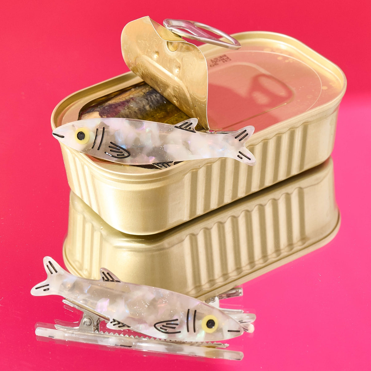 Gold can-shaped container with small fish-shaped objects on a pink background