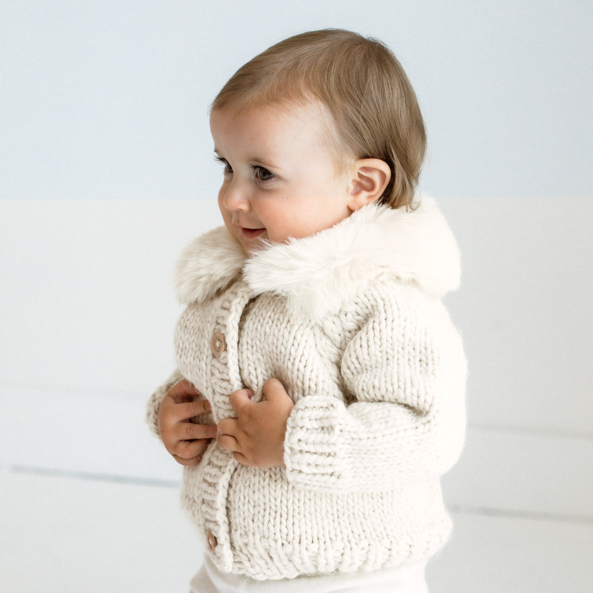 Child wearing a cream knitted jacket with fur trim on a light background