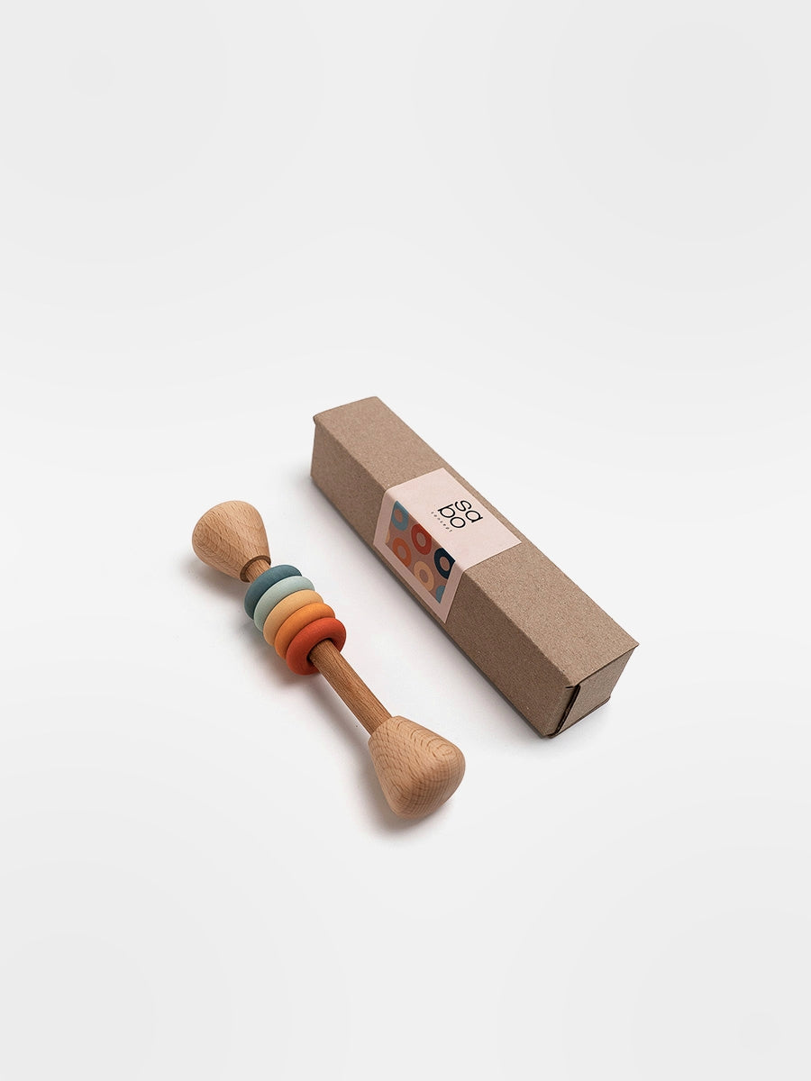 Wooden baby rattle with colorful rings next to its packaging on a white background