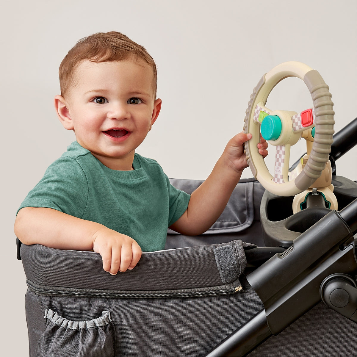 Child playing with a toy in a stroller against a plain background