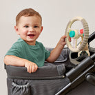 Child playing with a toy in a stroller against a plain background