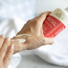 Hand applying lotion from a 'Earth Mama' bottle on a white background