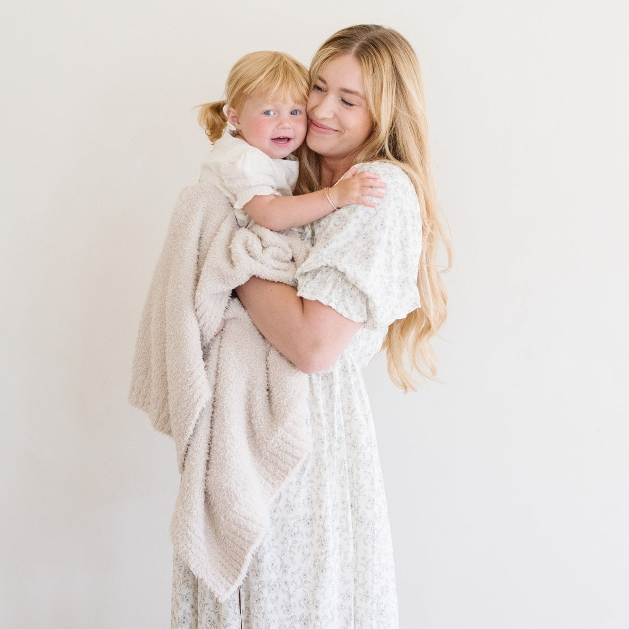 Woman holding a child wrapped in a beige blanket against a white background