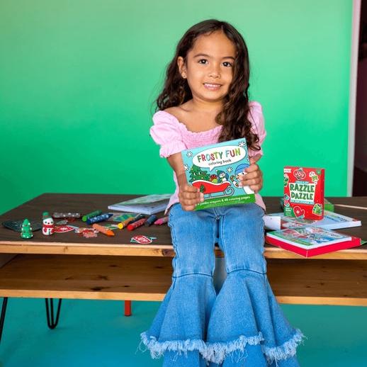 Young girl holding a book in a classroom setting with educational materials on a table.