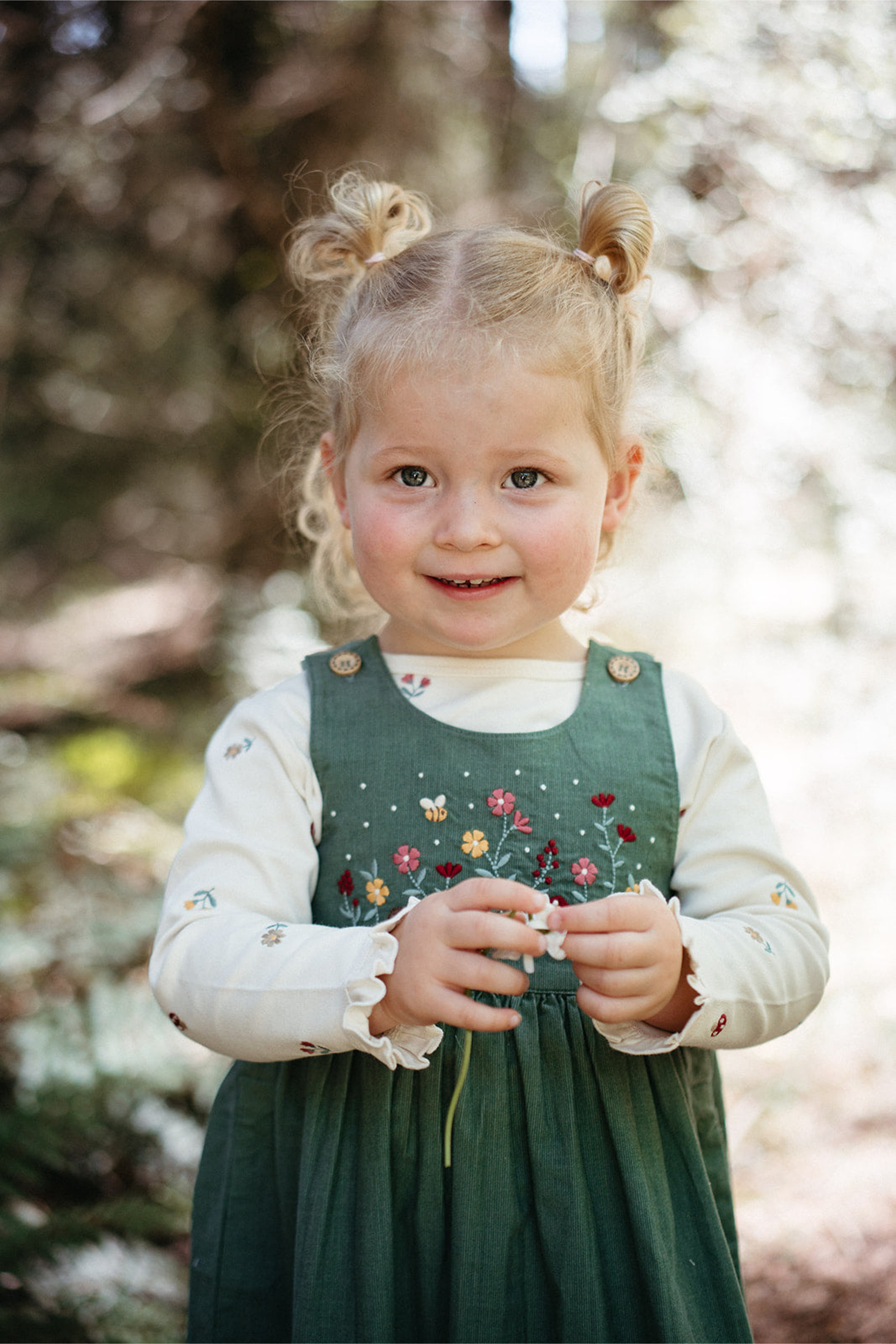 Young girl in a green dress with floral embroidery standing outdoors.