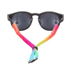 Black sunglasses with dark lenses and a bright rainbow gradient strap accessory attached to the sides, shown on a plain white background.