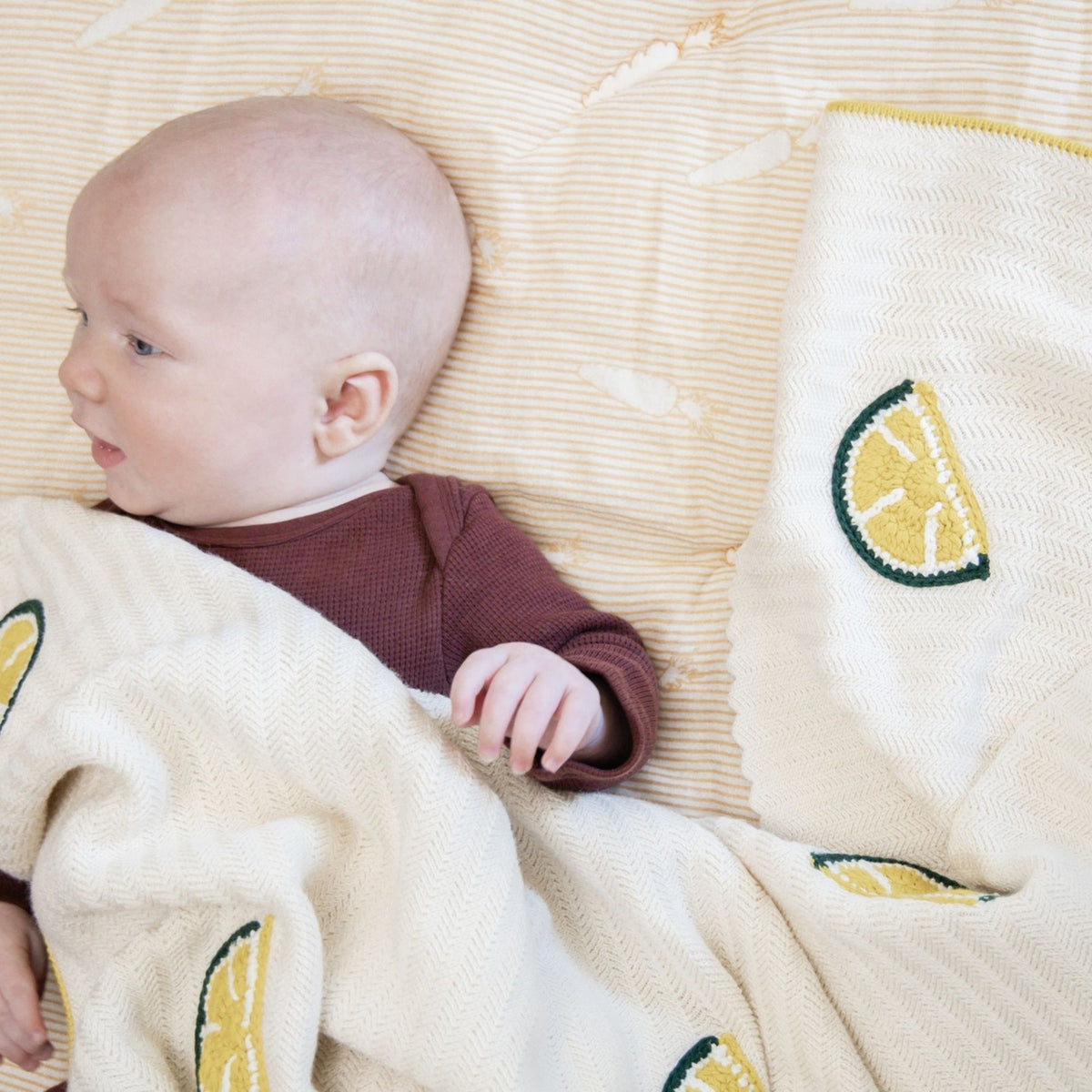 Baby lying on a textured surface with lemon-patterned blanket