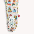 A close-up of a fabric product, likely a pouch or sleeve, featuring a whimsical pattern of illustrated animals sitting in colorful chairs and beds. The base fabric is a warm off-white/cream color, and a small red fabric tag with a white symbol is stitched on the side.