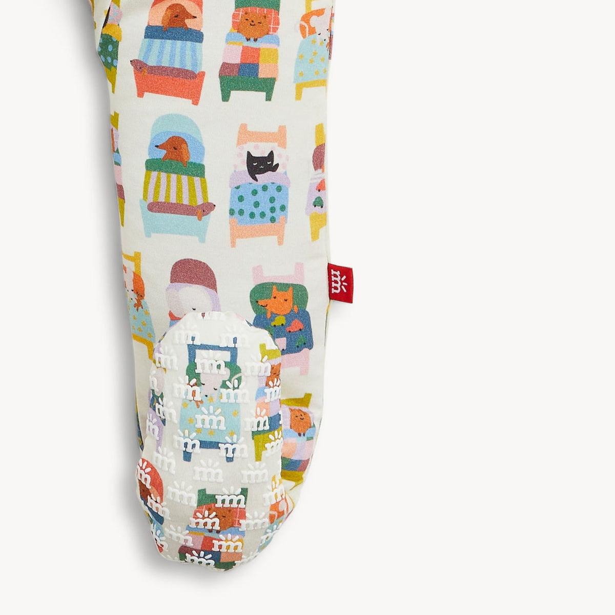 A close-up of a fabric product, likely a pouch or sleeve, featuring a whimsical pattern of illustrated animals sitting in colorful chairs and beds. The base fabric is a warm off-white/cream color, and a small red fabric tag with a white symbol is stitched on the side.
