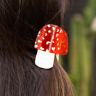 Red and white mushroom-shaped hair clip on dark hair with a blurred green background