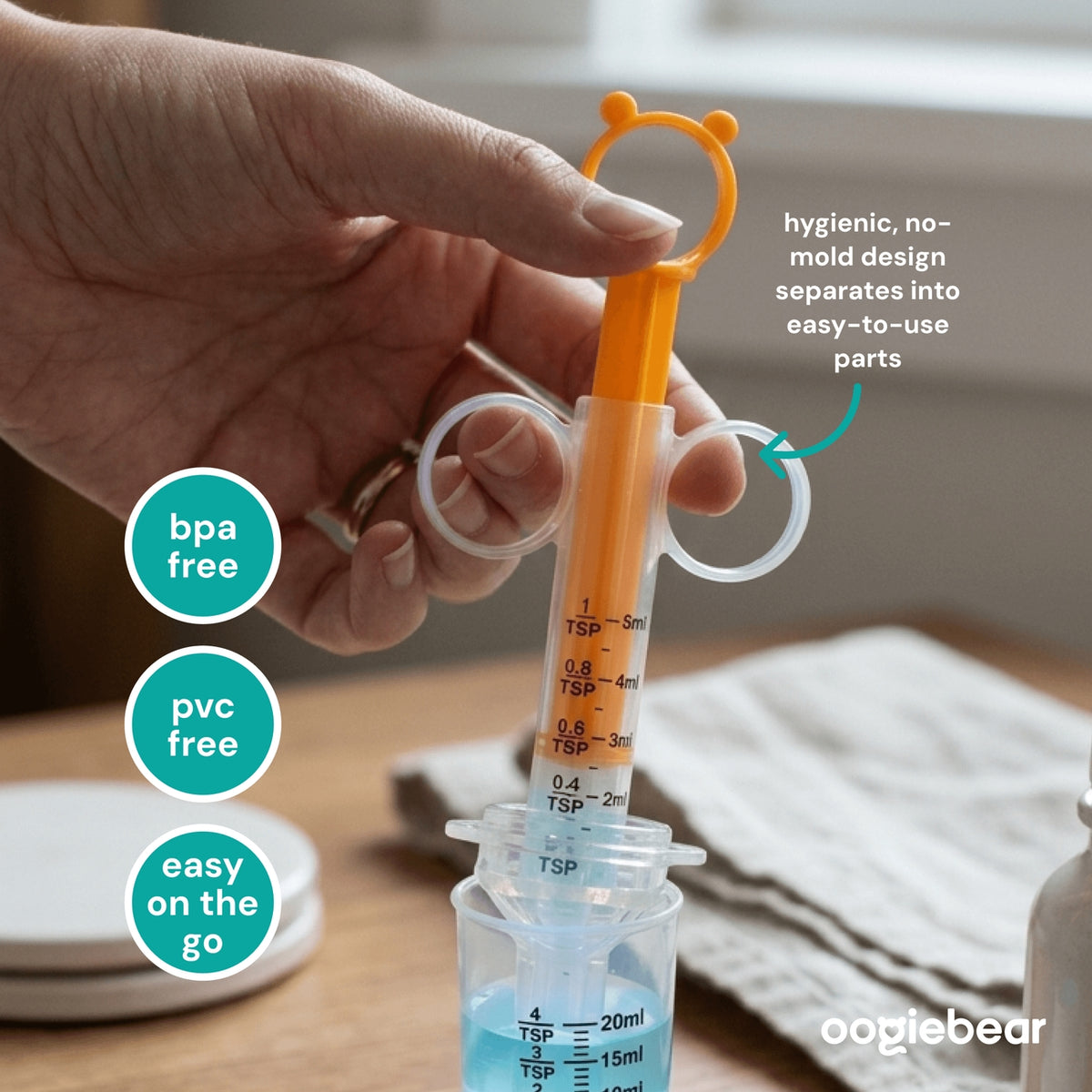 Hand holding a measuring syringe with text highlighting features, on a wooden surface.