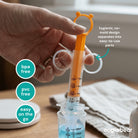 Hand holding a measuring syringe with text highlighting features, on a wooden surface.