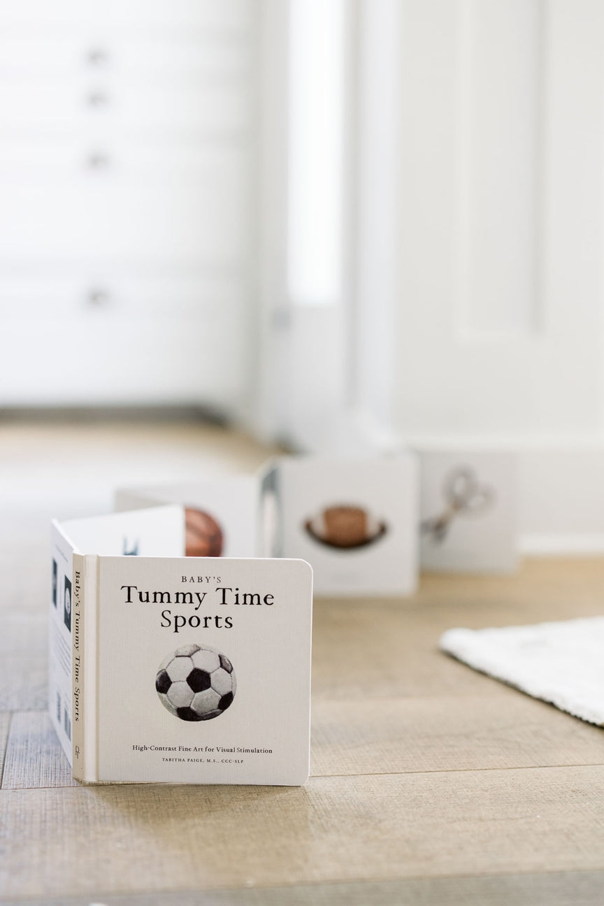 Children's book titled 'Tummy Time Sports' on a wooden surface with a blurred background