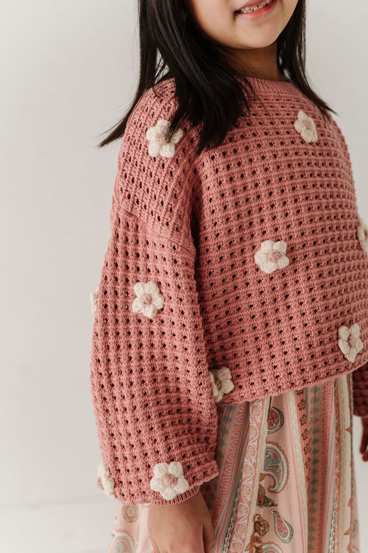 Child wearing a pink crochet sweater with flower patterns on a plain background