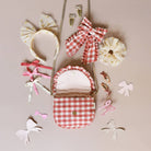 Collection of hair accessories including a red and white checkered bag, headbands, and ribbons on a beige background.