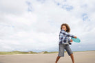 A child smiling and throwing a bright turquoise flying disc across a sandy beach under a cloudy sky.