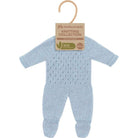 A light blue hand-knit baby jumpsuit for doll with a textured openwork pattern on the chest, raglan sleeves, and ribbed cuffs on the legs, shown against a plain white background with craft paper tag and clothing hanger.