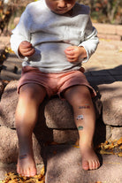 Child sitting on a stone step with temporary tattoos on their arms and legs.