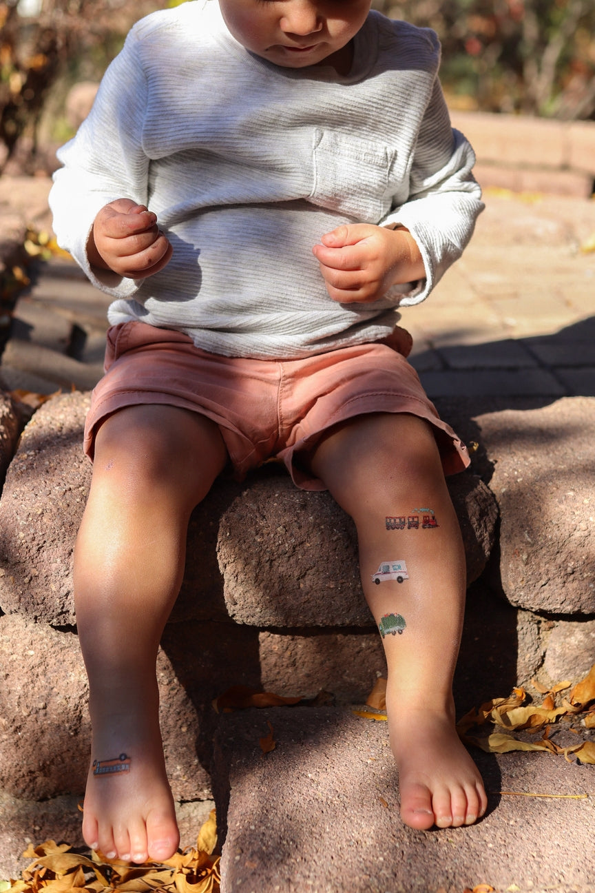 Child sitting on a stone step with temporary tattoos on their arms and legs.