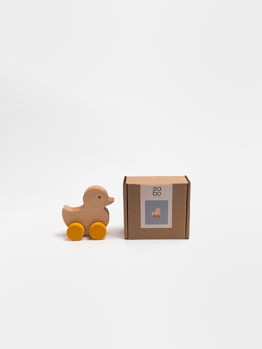 Wooden duck toy with wheels next to its packaging on a white background