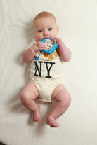 Baby wearing a onesie with 'NY' holding a toy on a white background