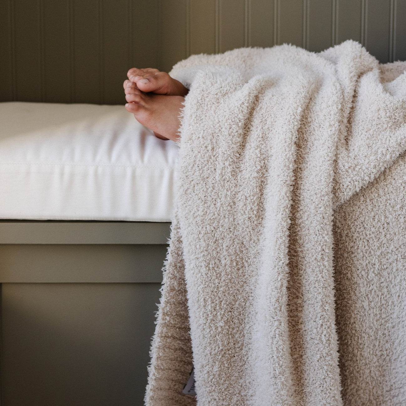 Person wrapped in a fluffy beige towel on a bed with a neutral background