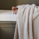 Person wrapped in a fluffy beige towel on a bed with a neutral background