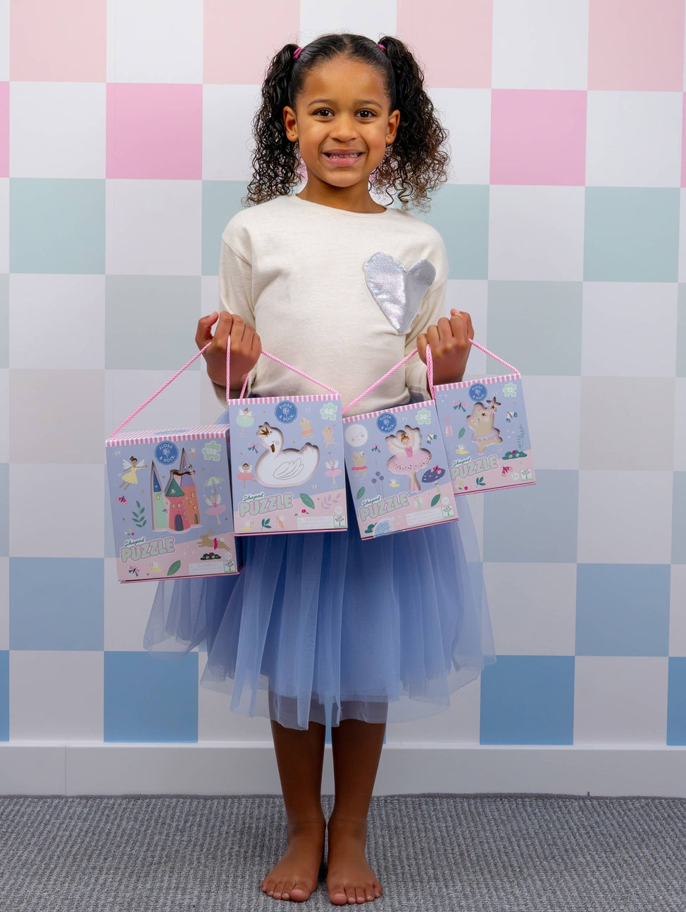 Young girl holding four small bags with cartoon designs against a checkered wall.