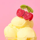Yellow ice cream with cherry toppings on a pink background