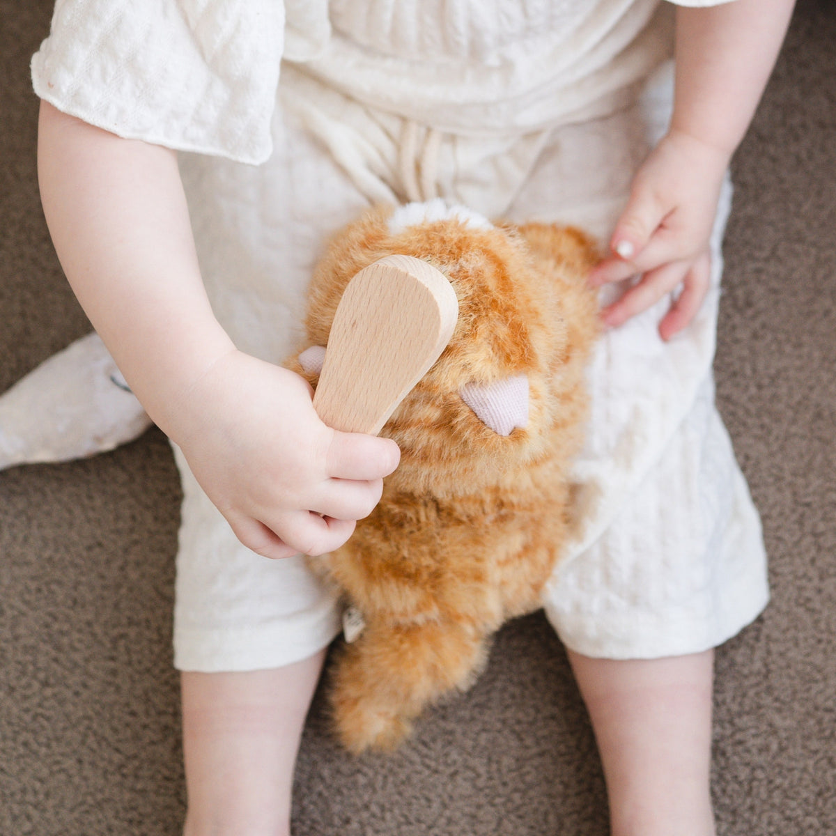 Child holding a plush toy and wooden comb on a neutral background