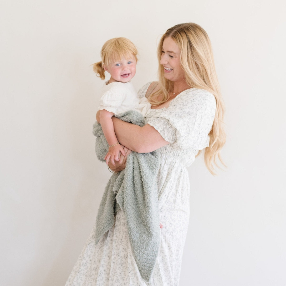 Woman holding a child wrapped in a blanket against a plain background