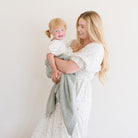 Woman holding a child wrapped in a blanket against a plain background