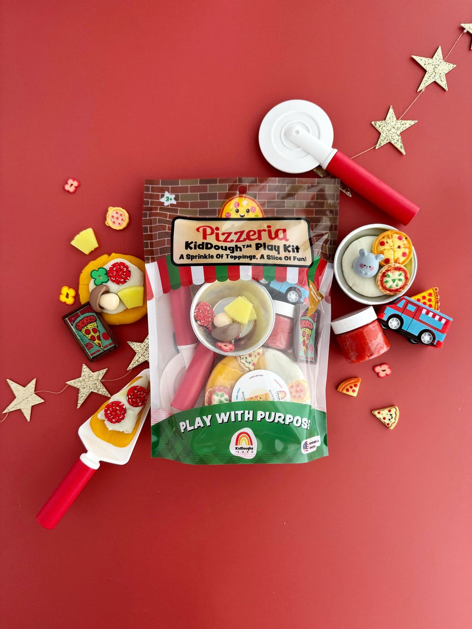 Pizzeria KidDough play kit with toy pizza cutter, play dough, and accessories on a red background.