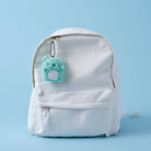 White backpack with a turquoise bear-shaped keychain on a light blue background