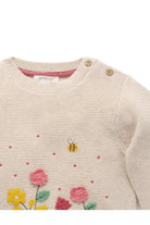 Close-up of a cream knit baby sweater with embroidered pink and yellow flowers, green leaves, a small bee, and pink dots, plus gold-toned shoulder buttons.