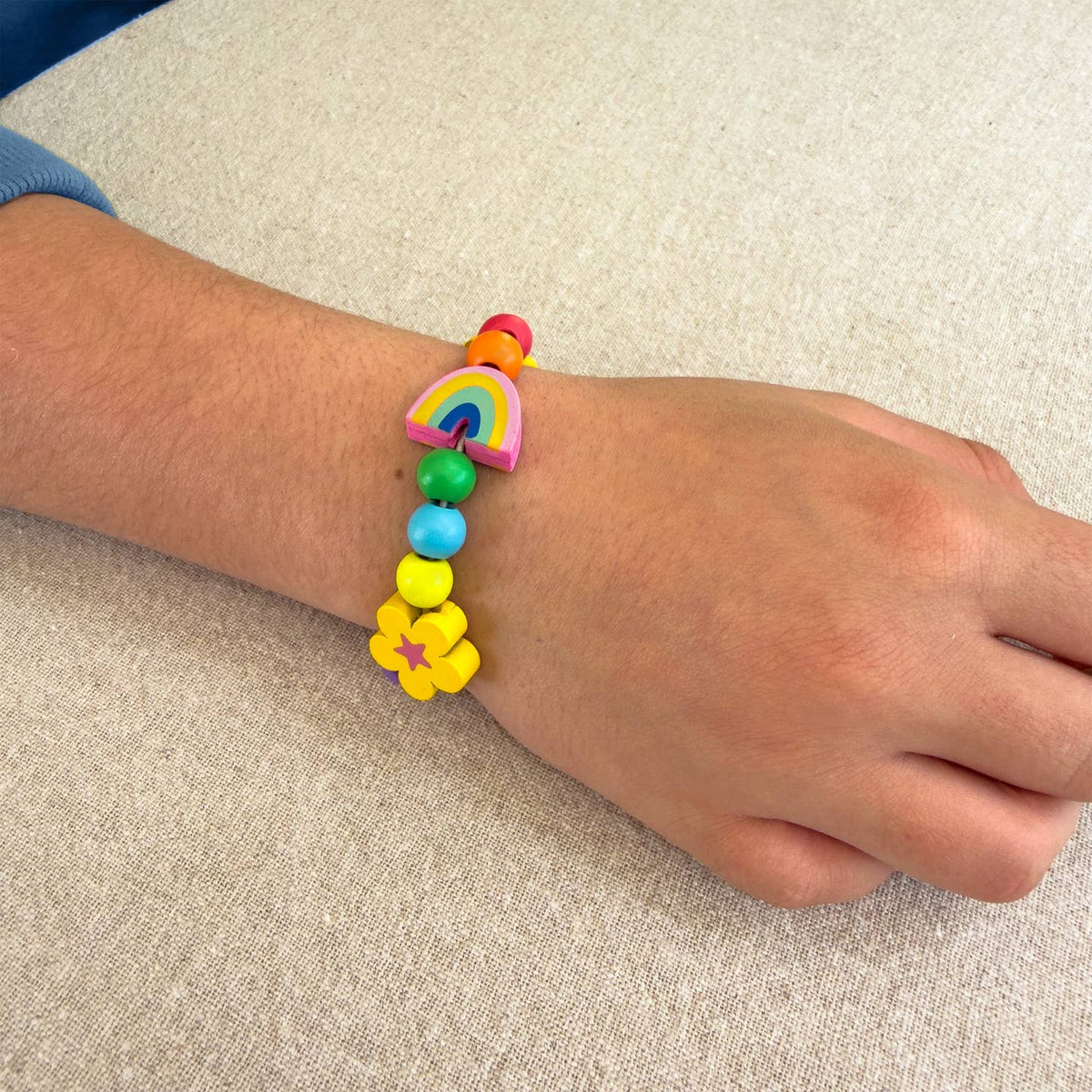 Colorful beaded bracelet with rainbow and flower designs on a wrist against a neutral background