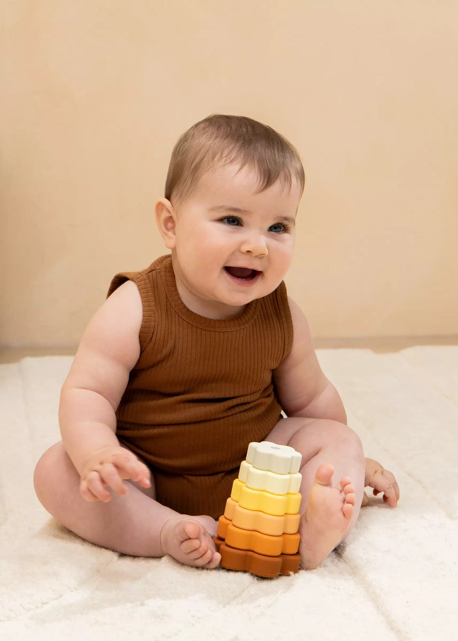 Baby sitting on a white blanket with a stack of colorful rings