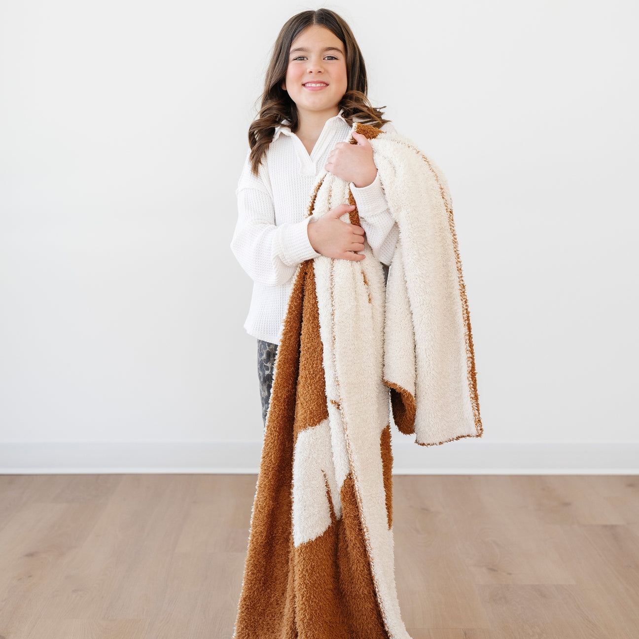 Child holding a brown and beige blanket against a white background