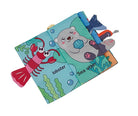 A baby tactile book featuring a sea otter and lobster theme, with a soft blue-green cover, a red lobster pull, and colorful fabric sensory toys attached along the spine, shown on a plain white background.