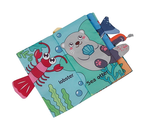 A baby tactile book featuring a sea otter and lobster theme, with a soft blue-green cover, a red lobster pull, and colorful fabric sensory toys attached along the spine, shown on a plain white background.