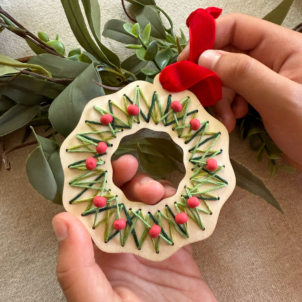 Handmade wooden ornament with green and red details held by a person against a natural background.