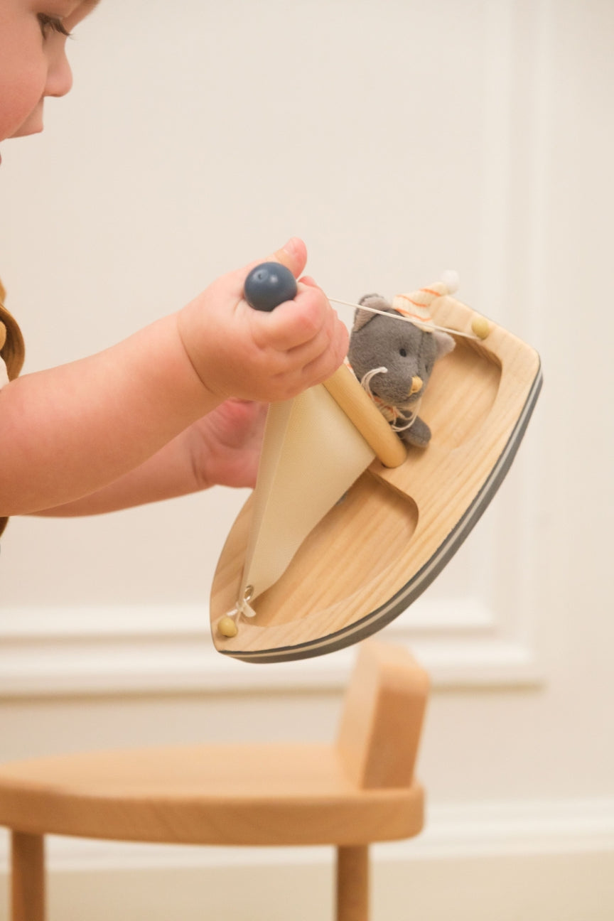Child's hand holding a wooden toy with a plush cat on a light background