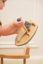Child's hand holding a wooden toy with a plush cat on a light background