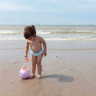 Child playing on a beach with a toy ball, wearing a light blue diaper.