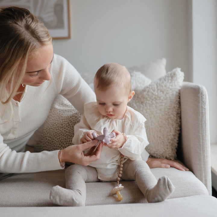 Woman and baby sitting on a couch with a toy, in a cozy indoor setting.