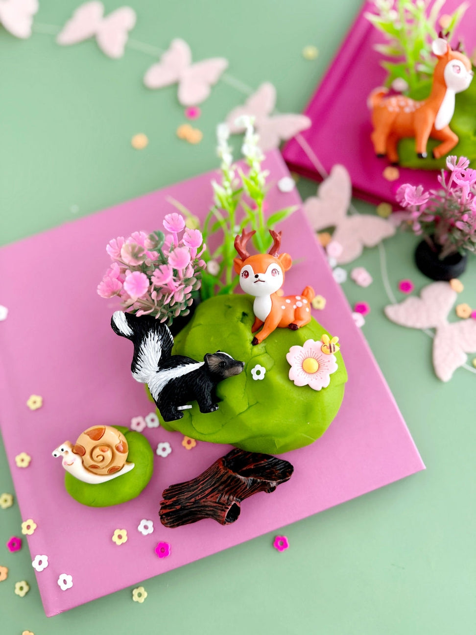 Decorative scene with animals and flowers on a pink card against a green background