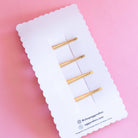 Set of gold hair clips on a white card with a pink background