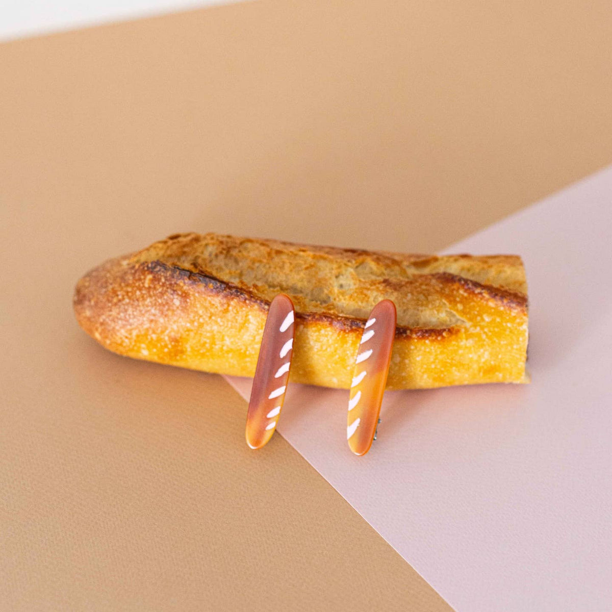 Loaf of bread with decorative pink and orange sticks on a two-tone background