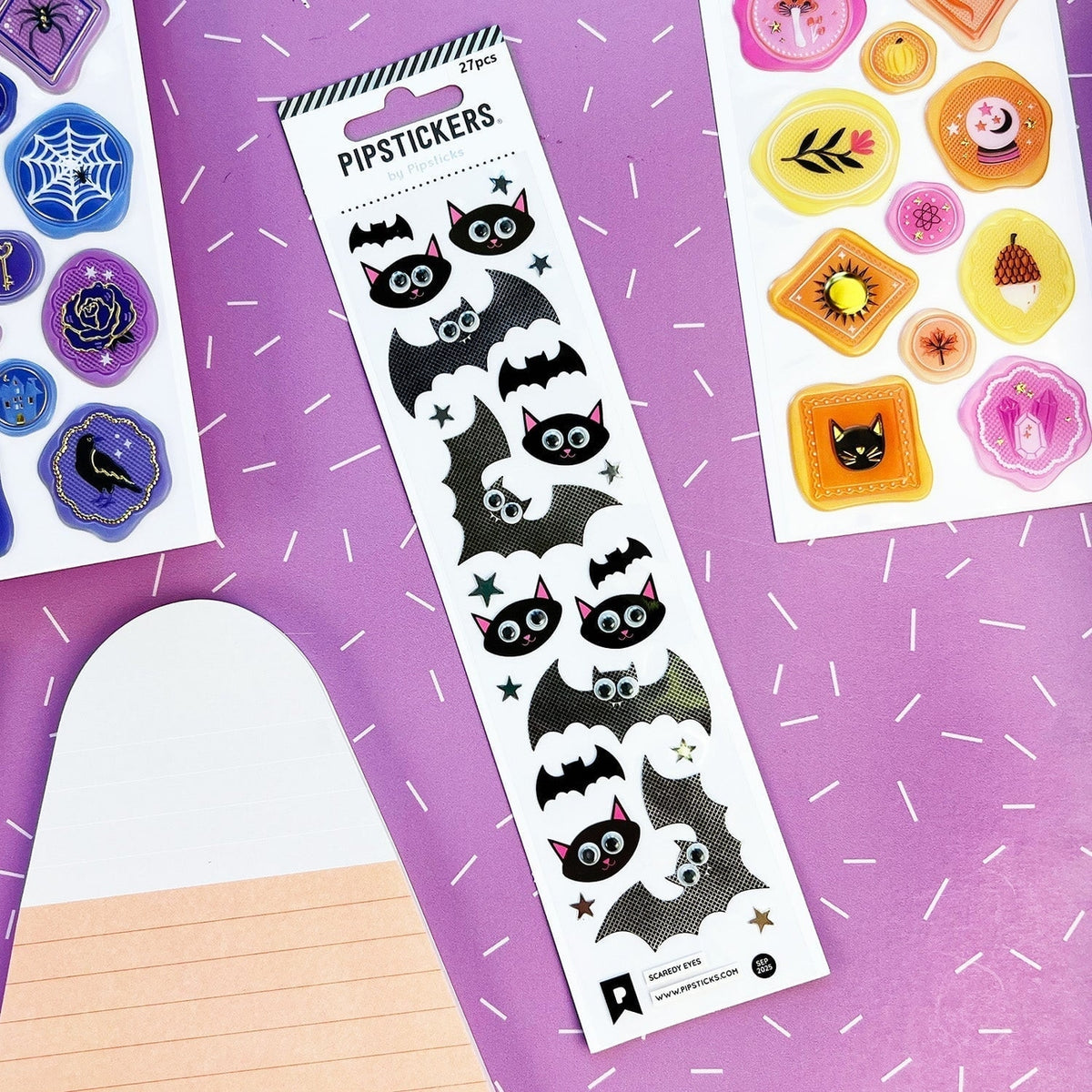 A sheet of Halloween-themed black bat stickers with white eyes and pink inner ears, displayed on a purple background alongside other sticker sheets.